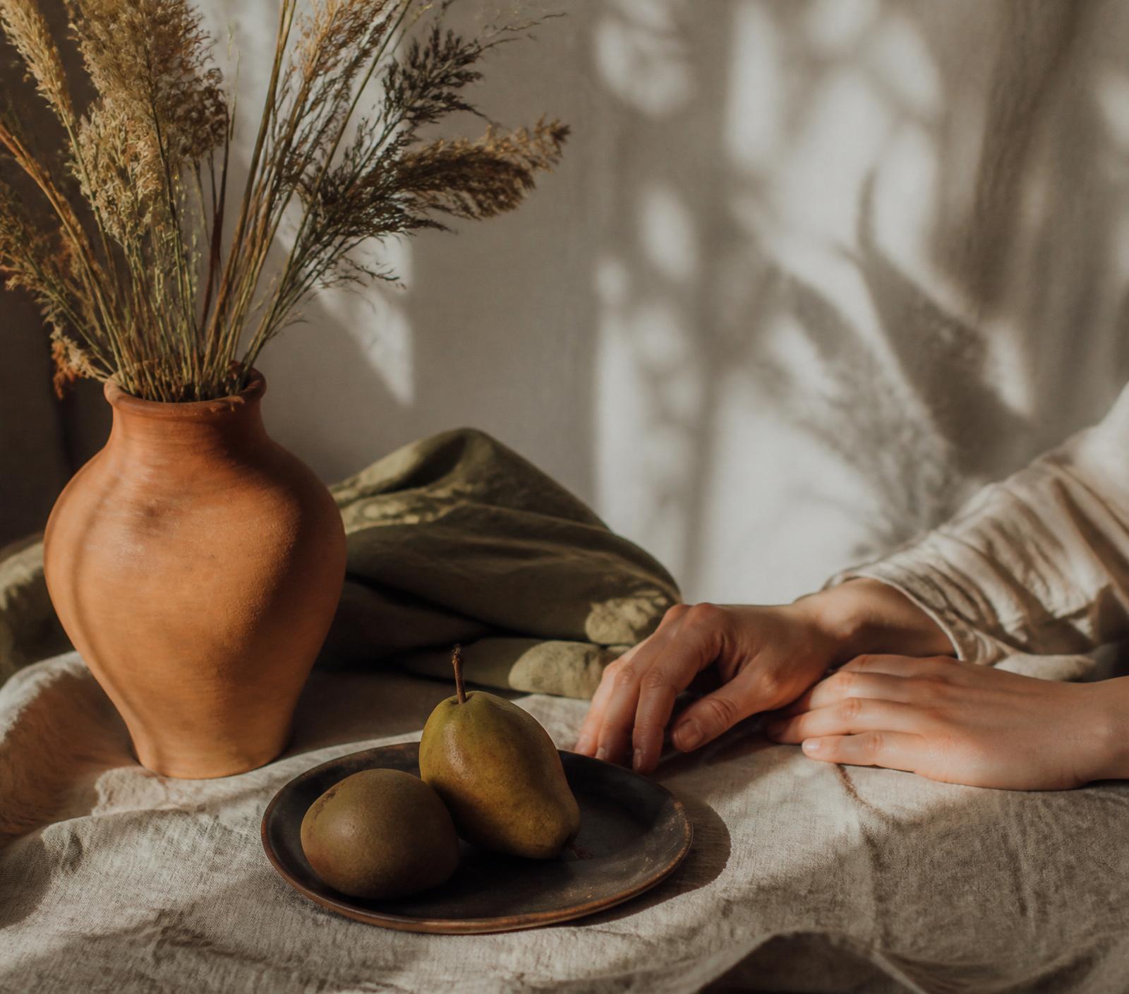 Warm sunlit still life with dried grasses in a terracotta vessel and linen drape